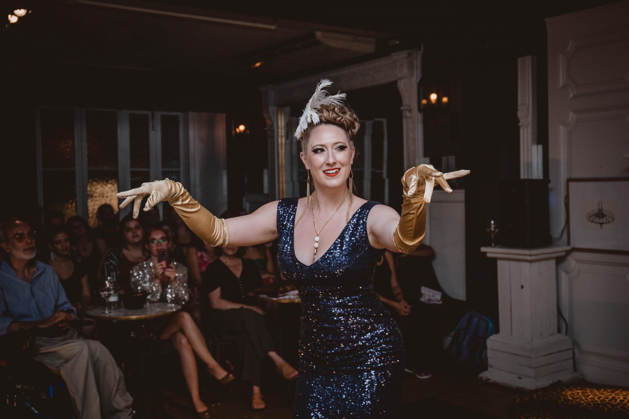 Lily La Rosa wears a blue sequin dress, gold gloves, a silver headdress, and poses with a big smile