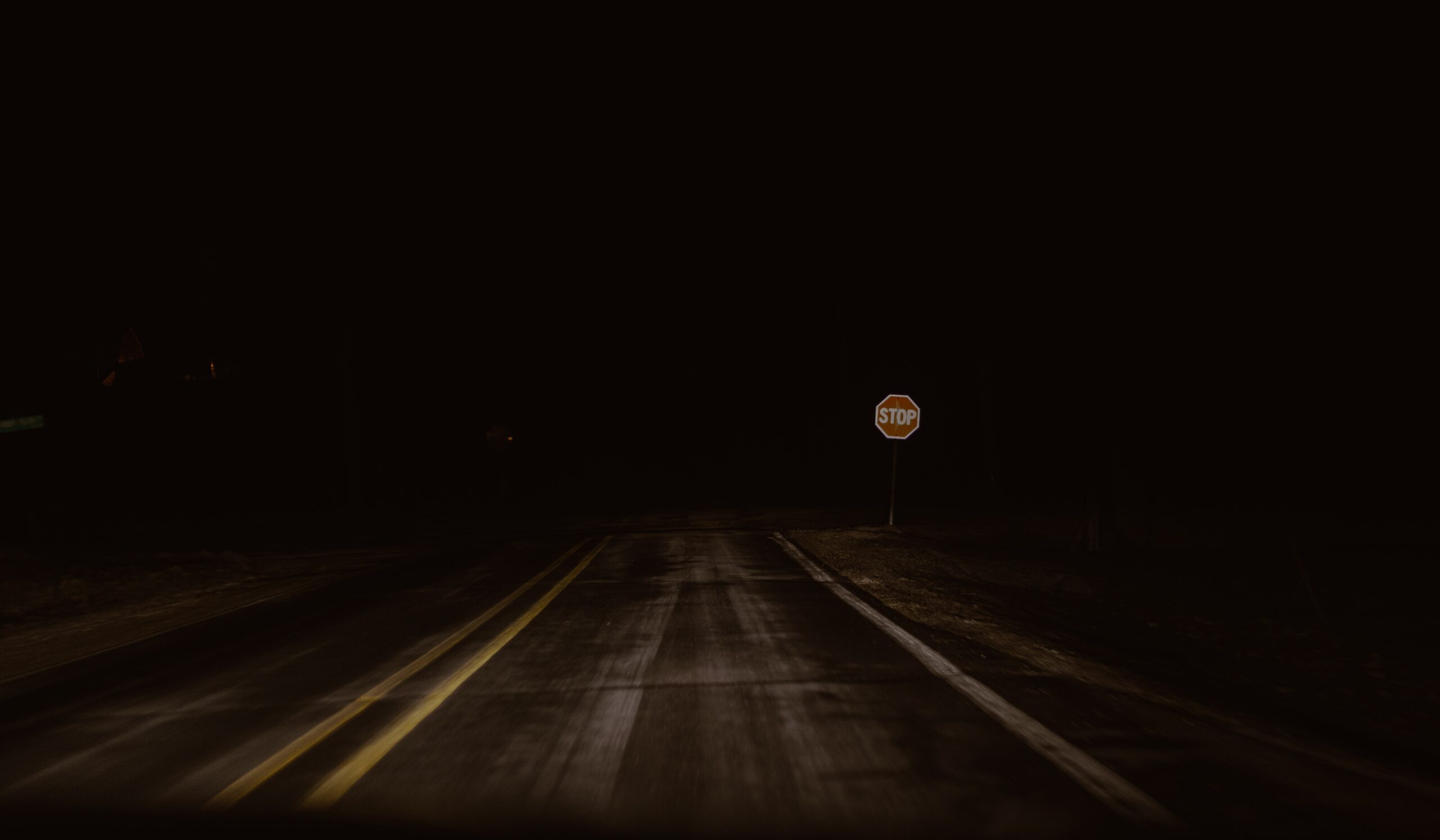 Road disappearing into dark night, with stop sign
